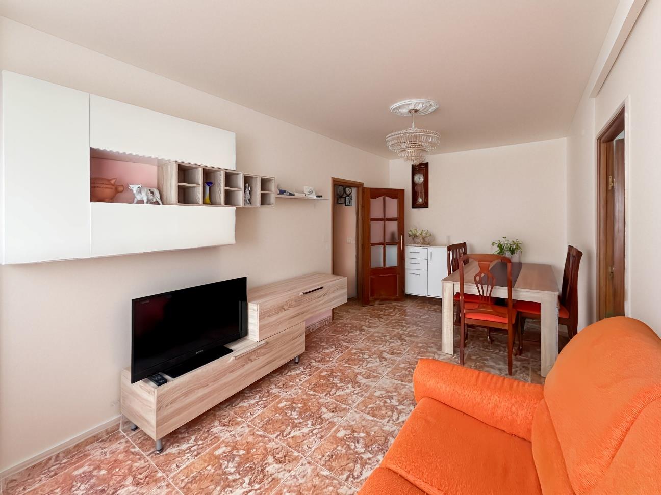 Salón con sofá naranja, suelo de mármol veteado y mueble bajo de madera clara con televisor