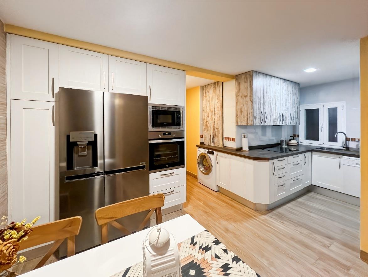 Cocina reformada con frigorífico americano, microondas empotrado y muebles blancos