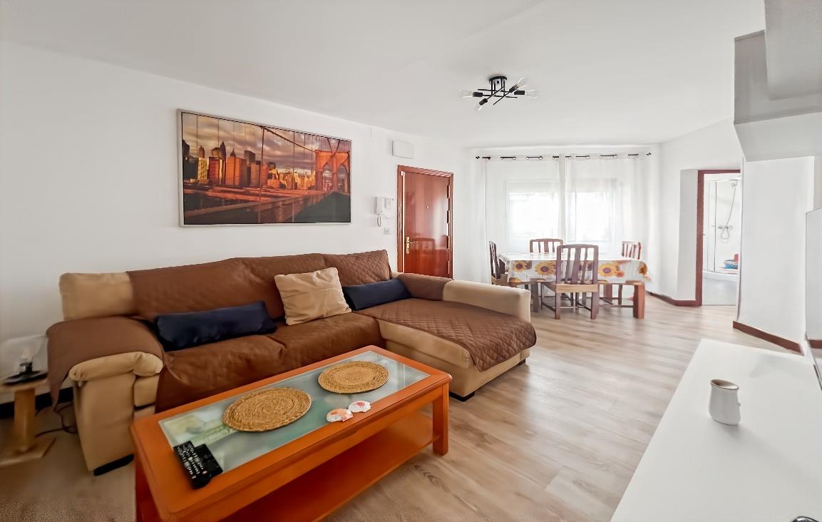 Salón amplio con sofá marrón, cuadro panorámico del puente de Brooklyn y comedor al fondo